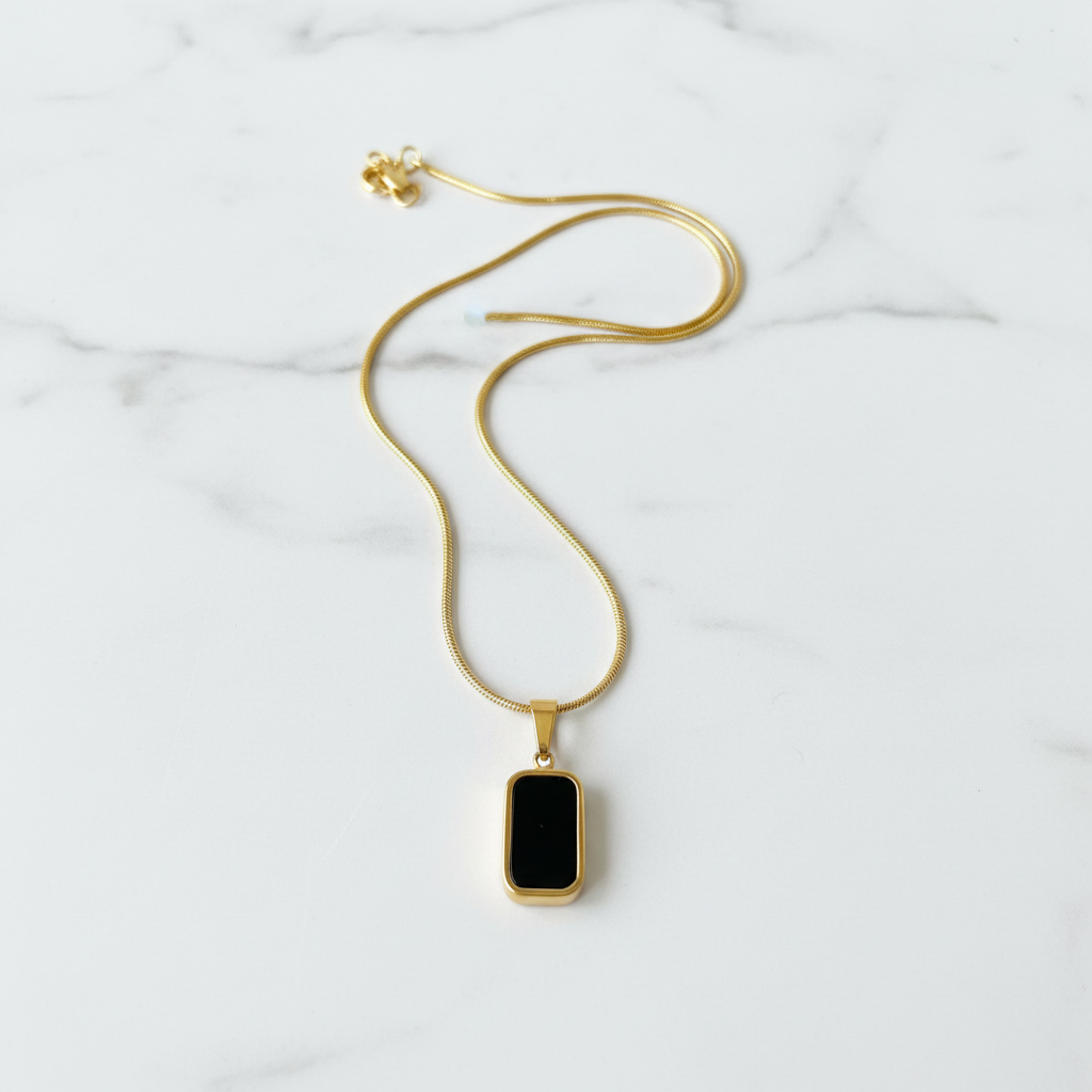 Black onyx gold pendant necklace flat lay on white marble